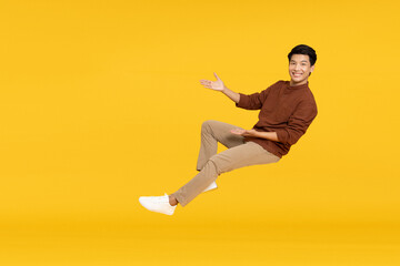 Happy cheerful young Asian man floating in the air isolated on yellow background, Presentation concept