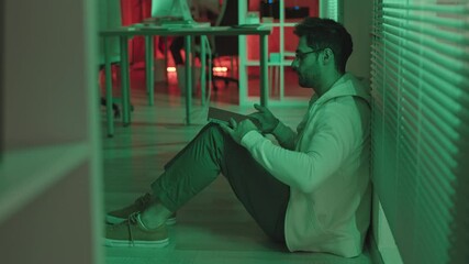 Wall Mural - stab shot with slowmo of tired male programmer with laptop sitting on floor in dark office with gree