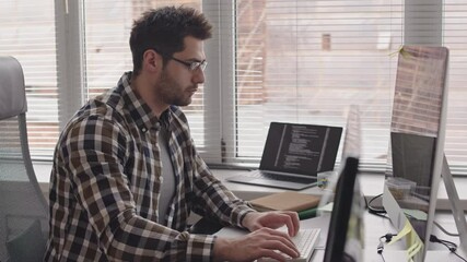 Wall Mural - side-view medium shot of bearded mixed-race programmer in casualwear and eyeglasses writing program 