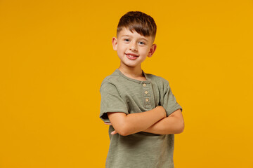 Little small fun smiling happy boy 6-7 years old wearing green casual t-shirt hold hands crossed folded isolated on plain yellow background studio portrait. Mother's Day love family lifestyle concept.