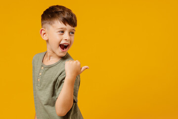 little small happy boy 6-7 years old in green casual t-shirt point thumb finger aside on workspace a