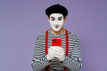 Charismatic Amazing Marvelous Ecstatic Young Mime Man With White Face Mask Wear Striped Shirt Beret Hold In Hand Use Mobile Cell Phone Isolated On Plain Pastel Light Violet Background Studio Portrait