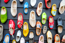Dutch Shoes - Klomps. A Lot Of Colorful Old Clomps Against The Background Of A Wooden Wall. Popular Souvenirs. Traditions Of Holland. Background