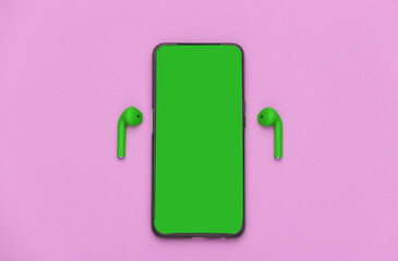 Smartphone with green screen and green headphones on purple background. Top view