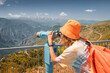 A woman on the observation deck looks through tourist telescope to the mountains or birdwatching. Travel and Tourism concept