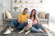 © Prostock-studio - Full length portrait of positive international couple with their pet dog sitting on soft carpet at home