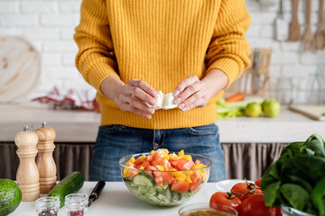 Wall Mural - Front view of female hands making salad cutting feta cheese in the kitchen