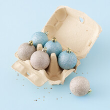 Creative Concept With Christmas Balls And Sequins In Egg Box On Pastel Blue Background, Top View. Minimal Christmas Holiday Concept Background.