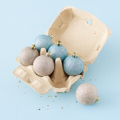 Creative concept with christmas balls and sequins in egg box on pastel blue background, top view. Minimal Christmas holiday concept background.