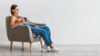 Leinwandbild Motiv Beautiful Caucasian woman sitting in armchair and enjoying cup of hot aromatic coffee against white wall, copy space
