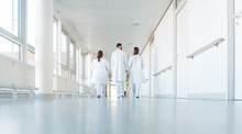 Three Doctors Walking Down A Corridor In Hospital Seen From Behind