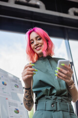 Wall Mural - low angle view of pleased businesswoman with pink hair holding smartphone.