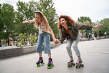 excited women holding hands while rollerblading in park.