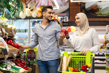 Wall Mural - Muslim Couple Enjoying Grocery Shopping Together Buying Vegetables In Supermarket