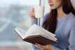 © VICHIZH - woman reading a book near the window with a cup of drink rest