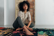 © Daniel - Pensive young multiracial smiling woman sitting on floor looking away. Copy space.