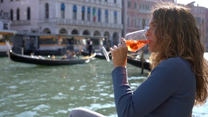 Wall Mural - Girl holds in hand and drinks a glass of Spritz, in the city of love - aperitif, alcoholic drink Spritz Camapari or Aperol - typical drink of Venice made with  white wine, orange - Rialto bridge 
