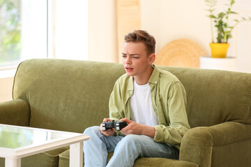 Poster - Displeased teenage boy playing video game on sofa at home