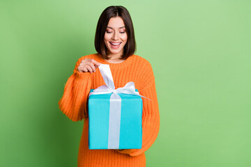 Poster - Portrait of attractive curious funny cheerful girl opening festal giftbox isolated over vibrant green color background