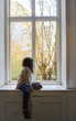 © JORGE CORCUERA - lonely girl sitting on the side of a large antique window looking out onto the street