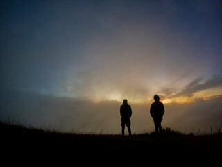 Silhouettes of two campers watching the sunrise in the mist from top of 'Le Pouce' mountain