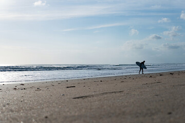 surfer walking along the kuta beach, bali