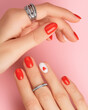 Manicured womans hands with rings on pink background. Fashionable red nail design with heart