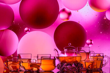 Wall Mural - transparent glass teapot and cups with tea and oily drops on colorful background 