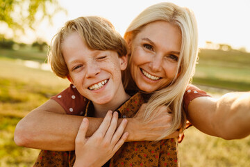 white mother and son smiling while taking selfie photo on field