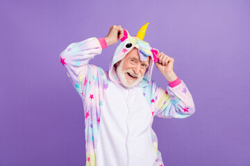 Poster - Photo of amazed childish man pensioner unicorn sleepwear dancing arms hands hood smiling isolated violet color background