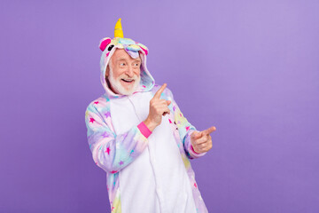 Poster - Photo of funny amazed man pensioner unicorn sleepwear looking pointing fingers empty space smiling isolated violet color background