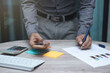 © thithawat - business man working on table at office. man hand use pen pointing on business graph or chart with keyboard and using smartphone to analysis statistics and strategy for investment success target.