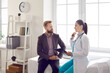 © Studio Romantic - Eembarrassed male patient discusses treatment with his doctor during meeting at hospital office. Young serious female doctor tells about diagnosis to her patient sitting on couch by window.