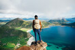 © BublikHaus - Young adventurer stand on top of mountain peak after long exhausting hike, wear athletic outdoor outfit. Hiker with backpack look over steep cliff on epic lofoten archipelago in norway