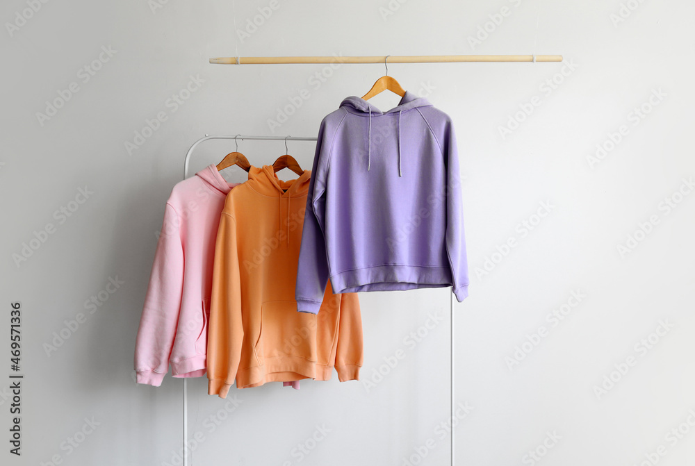 Modern hoodies hanging on rack and light wall