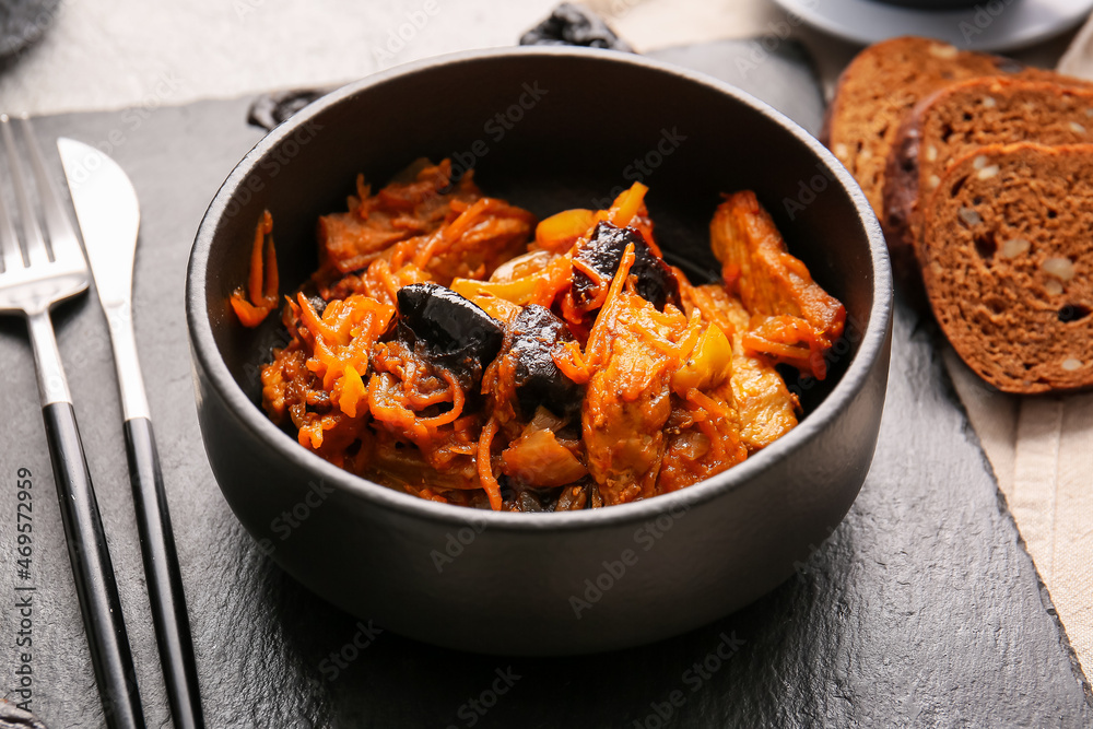 Dark board with delicious beef stew and prunes in bowl on light table, closeup