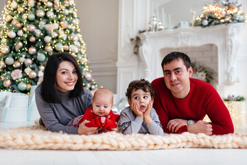 A happy family with children lies on the floor near the Christmas tree.