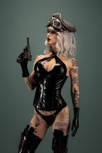 Pretty Tattooed Young Woman Wearing Latex Lingerie, Cap And Gun