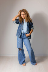 Wall Mural - young curly haired woman with blue eyes in a full length denim suit. model poses in the studio. space for text. High quality photo