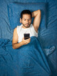© Narayan - latin man using cell phone on blue bed, cell phone concept