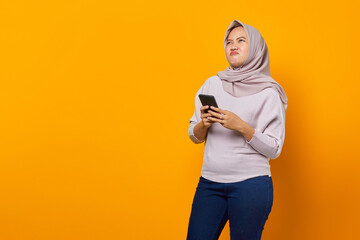 Portrait of beautiful asian woman holding mobile phone and looking aside on yellow background