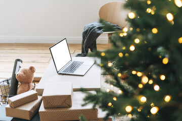 Opened laptop with white screen on table in living room with decorated Christmas tree, Online shopping concept