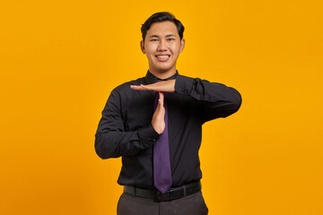 Portrait of young Asian businessman showing timeout gesture on yellow background