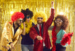 © Studio Romantic - Crazy and happy multiethnic friends have fun dancing and laughing at a bright party. African american and caucasian men and women in colored bright glasses and wigs dance on a golden background.