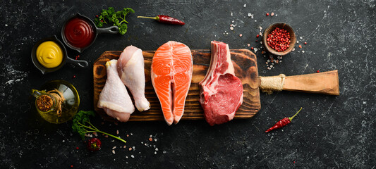 Wall Mural - Mix of steaks: salmon, beef, pork and chicken, on a dark stone background. Top view. Organic food.