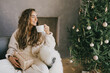 © polinaloves - Young woman drinking hot coffee or cocoa sitting on couch in cozy room with Christmas tree. Winter holidays.
