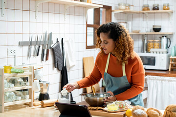 young beautiful african american woman in kitchen learning online virtual cooking class from tablet 