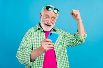 Sticker - Photo of cheerful positive cool old grandparent look phone winner raise fist luck isolated on blue color background