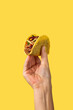 Hand holding a Mexican taco beef on yellow background