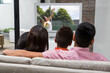 © vectorfusionart - Rear view of family sitting at home together watching tennis match on tv